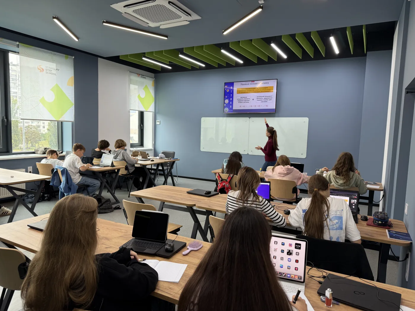 Клас на уроці: учні з планшетами за партами, вчителька біля екрана