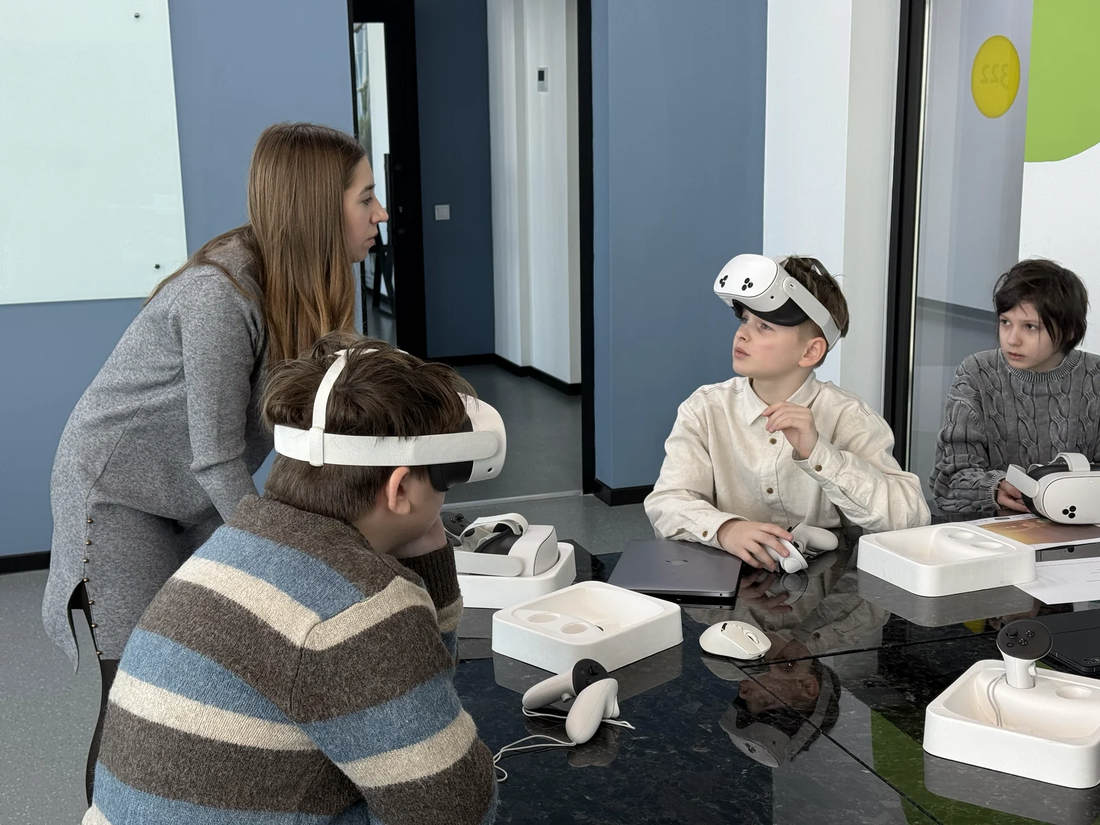 Учні у VR-шоломах із контролерами за столом, учителька поруч